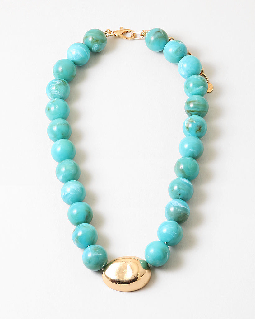 Chunky turquoise beaded necklace with a large oval gold bead and gold clasp on a white background