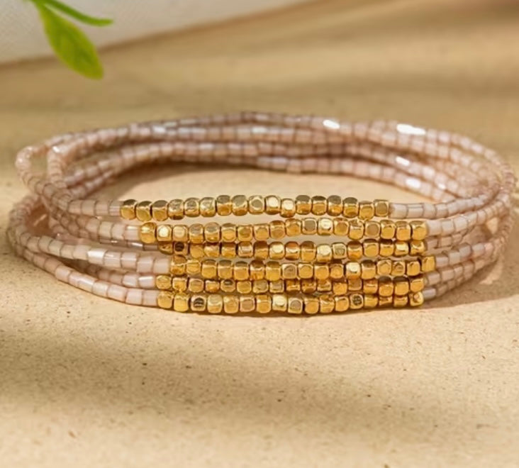 Stack of beaded bracelets with gold and beige beads on a beige surface.