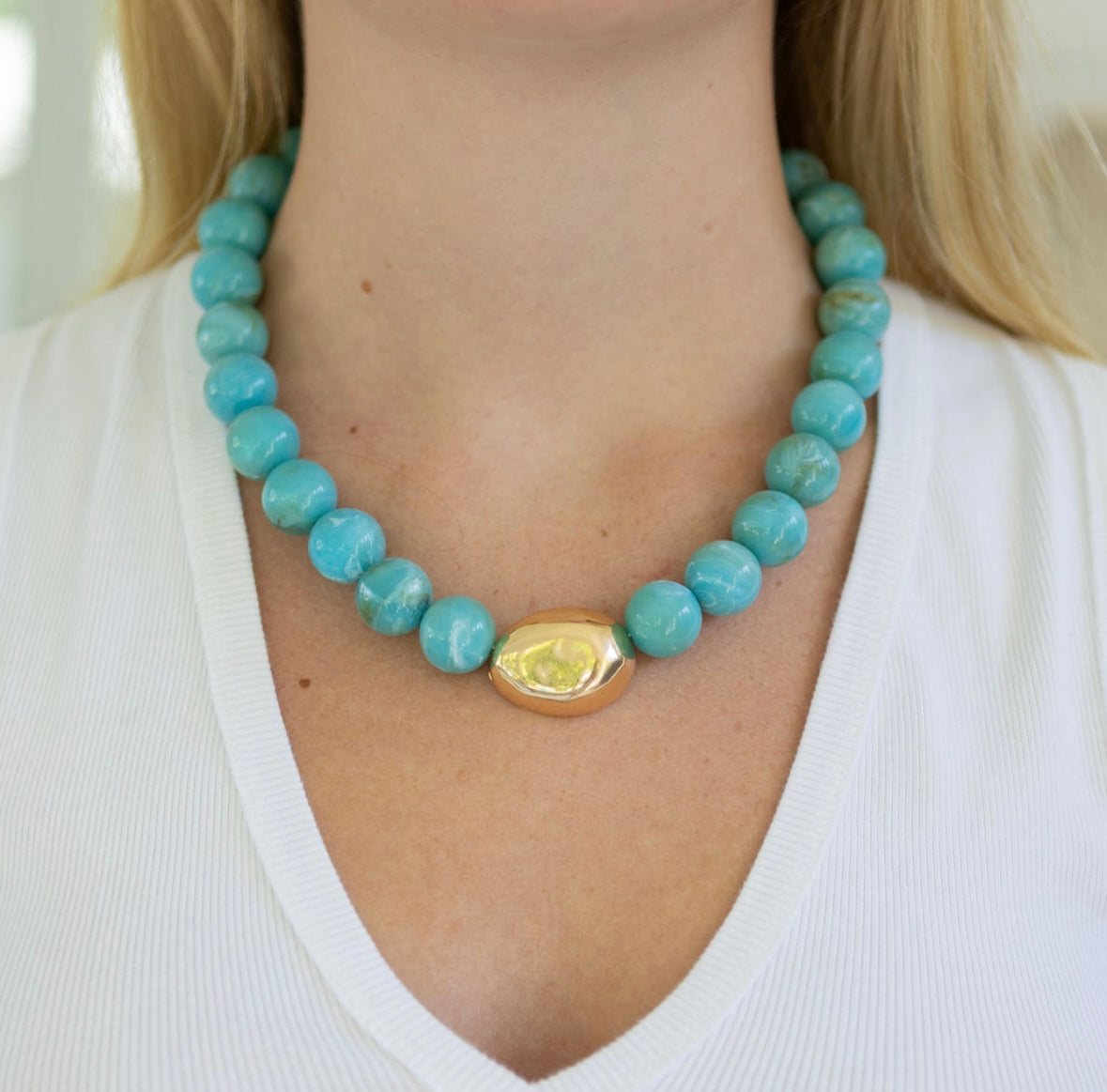 Chunky turquoise beaded necklace with a gold accent bead worn by a person in a white shirt.