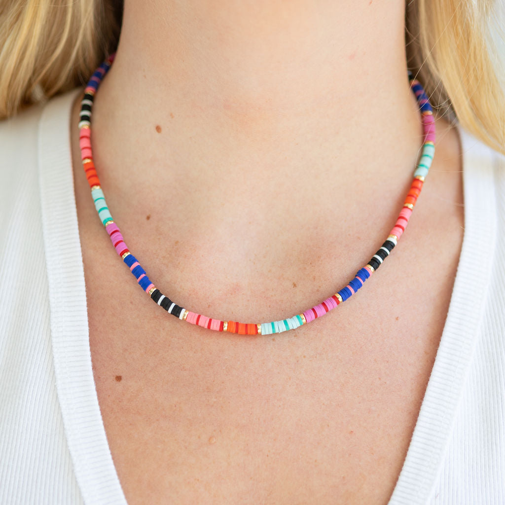 Colorful pink, red, black and gold beaded necklace worn by a person with a white background