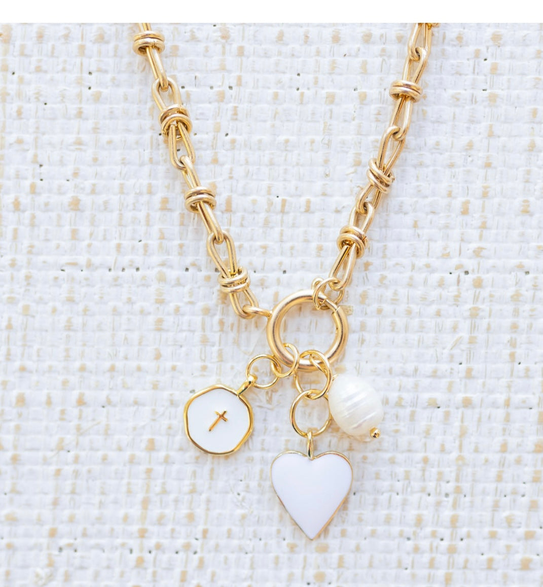 Picture of gold toggle chain with a white heart charm, white disc charm with a cross at the center and a fresh water pearl charm.