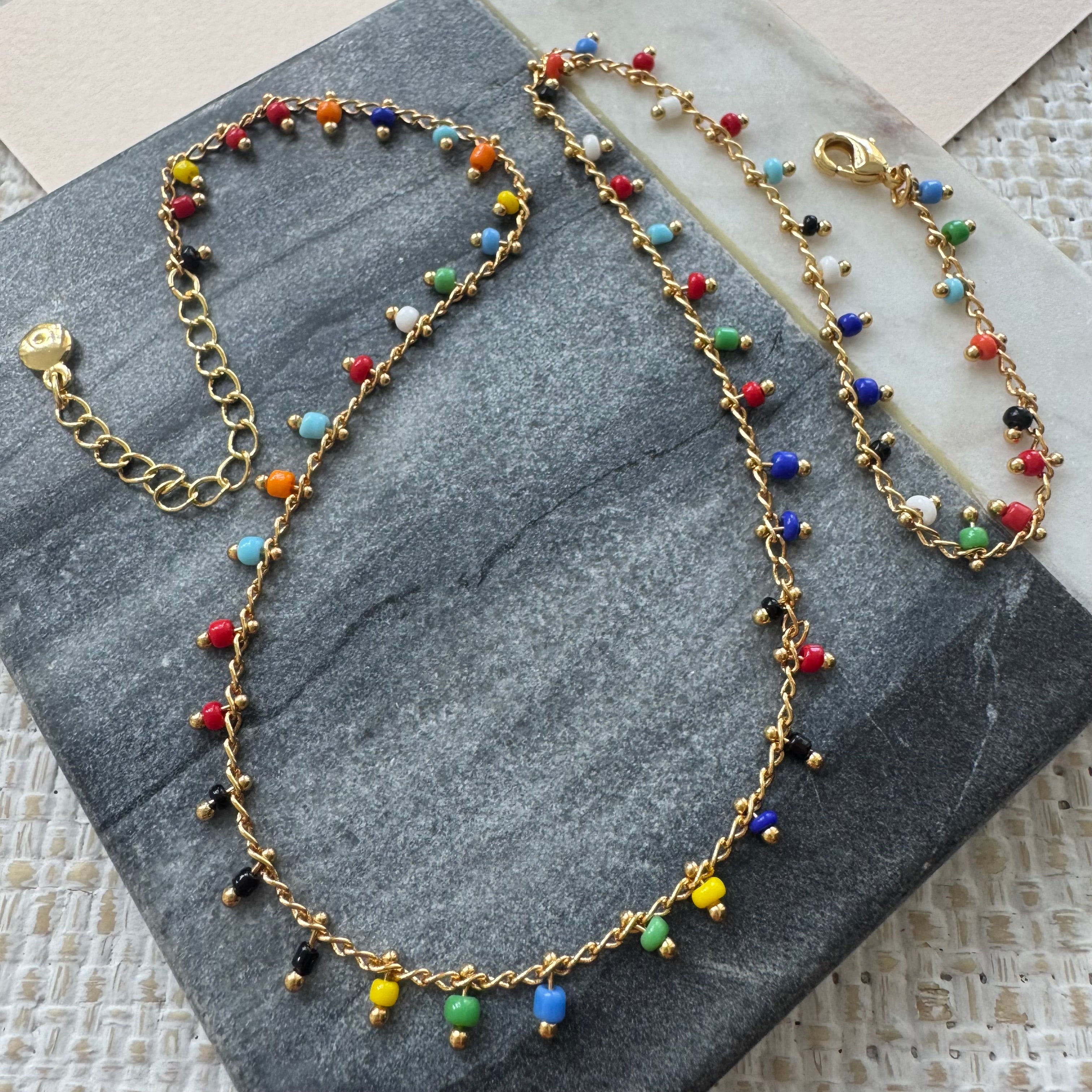 Delicate gold chain necklace with colorful beads on a gray stone surface