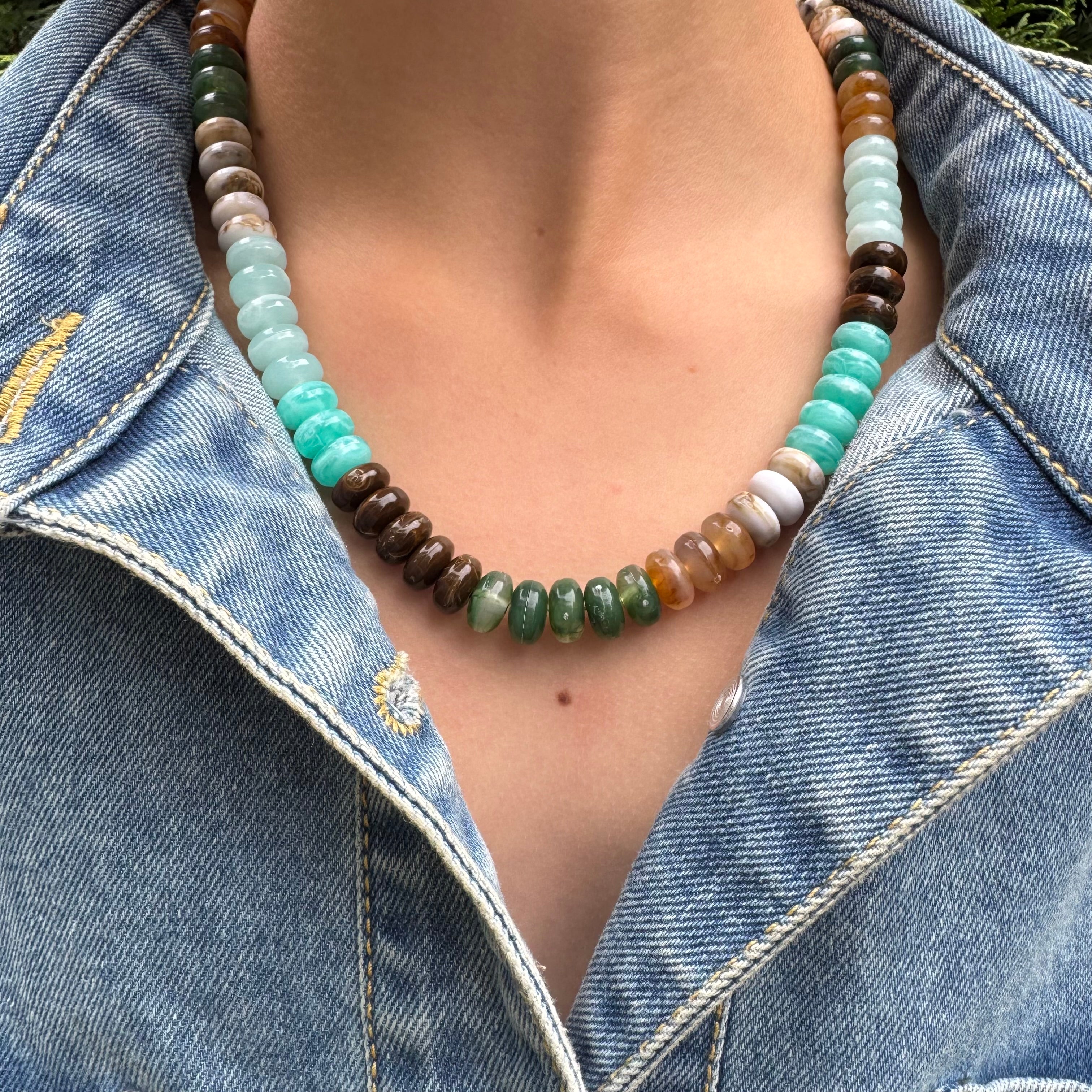 Necklace with multicolored turquoise, green and brown beads worn by a person in a denim jacket.