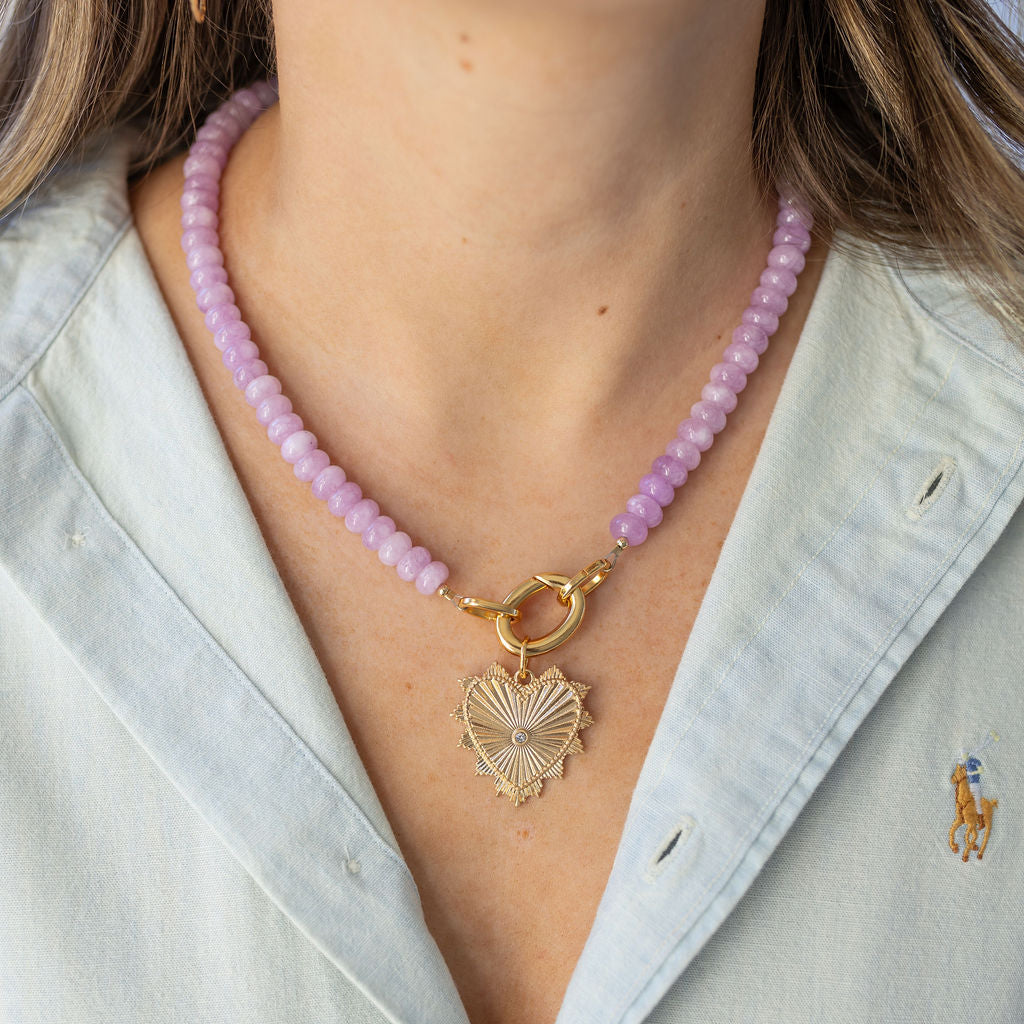Model wearing a front clasping pink quarts beaded necklace with a textured golden heart pendant