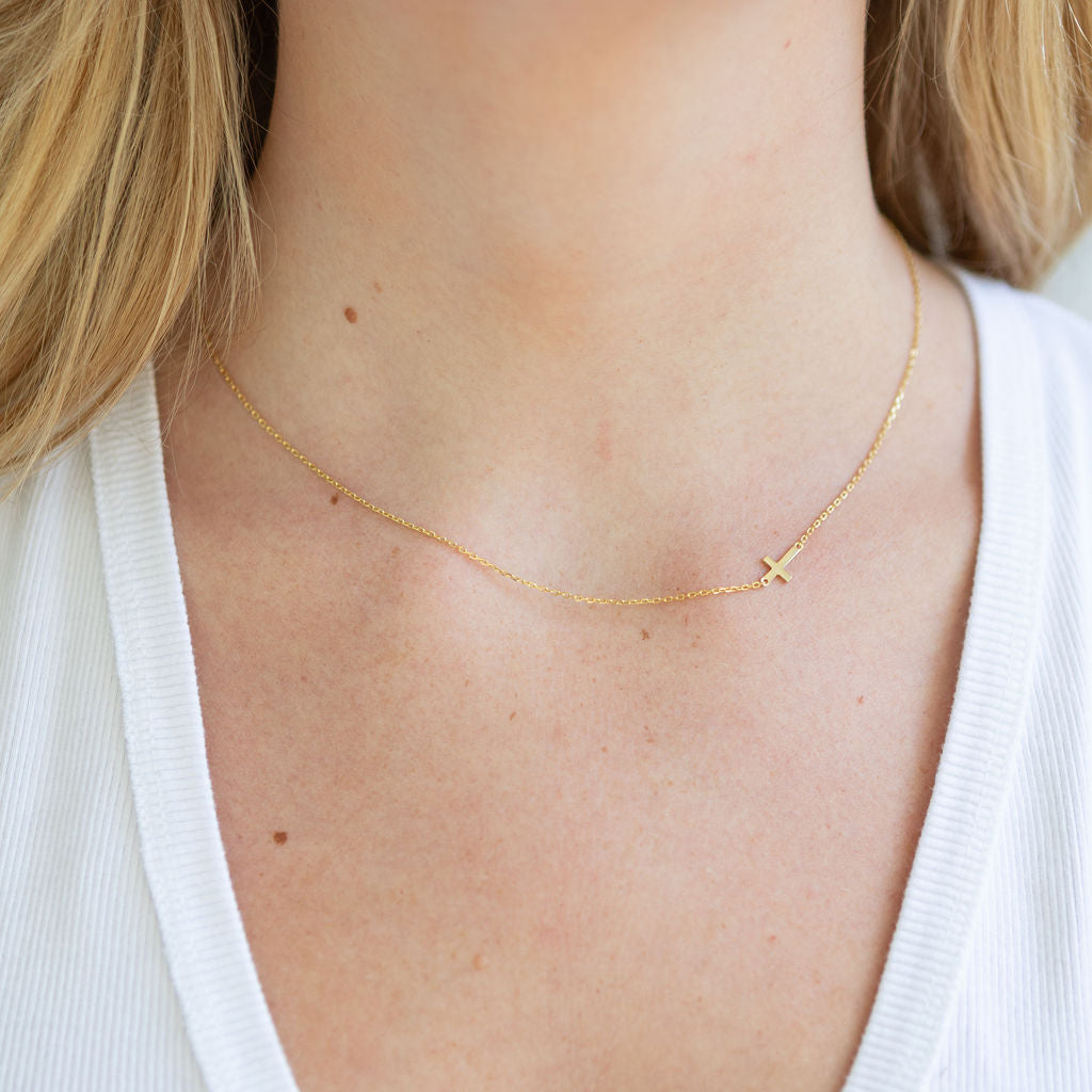 Gold necklace with a small cross pendant on a person wearing a white top.