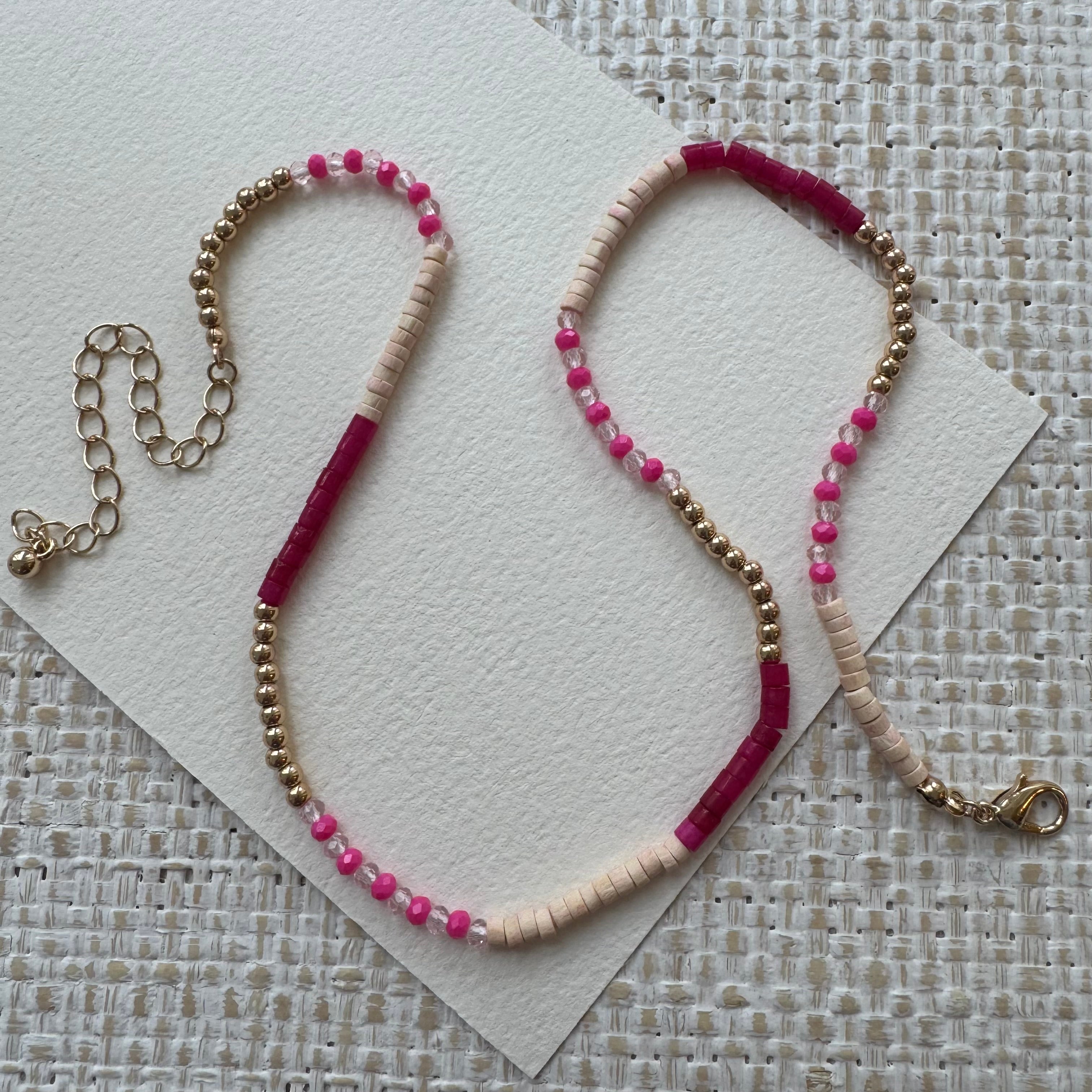Necklace with pink, gold, white, red and beige beads on a textured surface