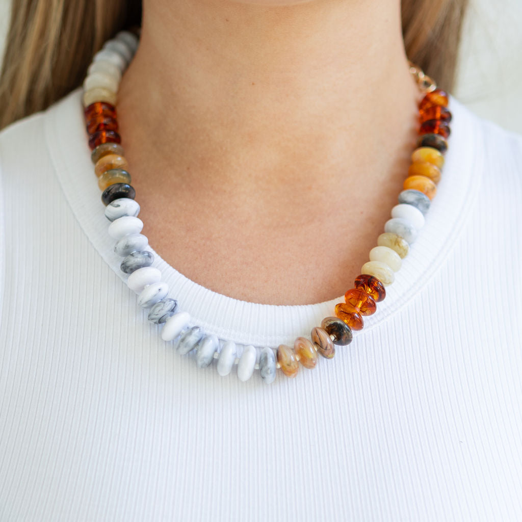 Necklace with multicolored gray and amber beads worn by a person on a white background