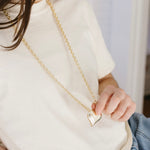 Picture of a woman wearing a long gold chain necklace with a large gold Puffy heart necklace.