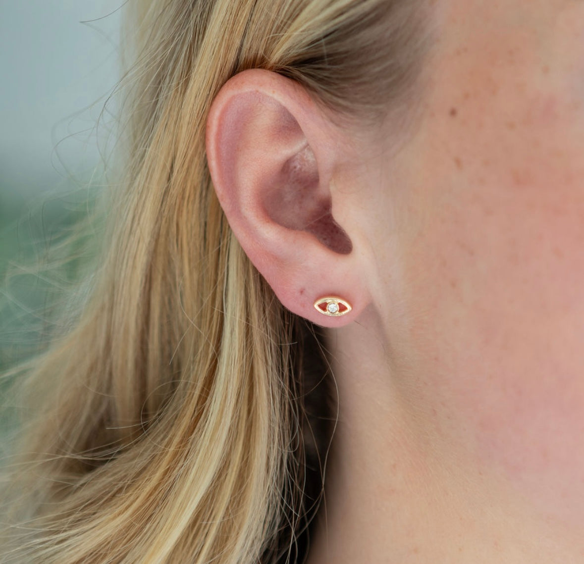 Close-up of an ear wearing a small evil eye earring with a blurred background