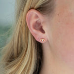 Close-up of an ear wearing a small evil eye earring with a blurred background