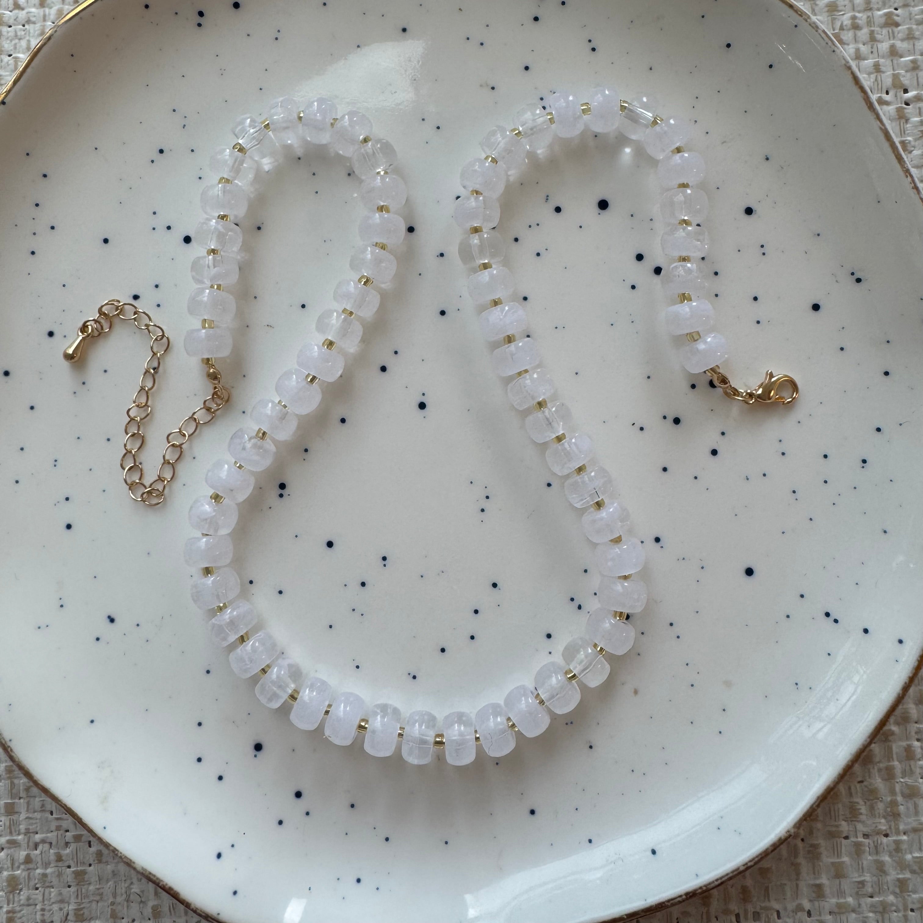 White beaded necklace with gold accents on a speckled ceramic plate