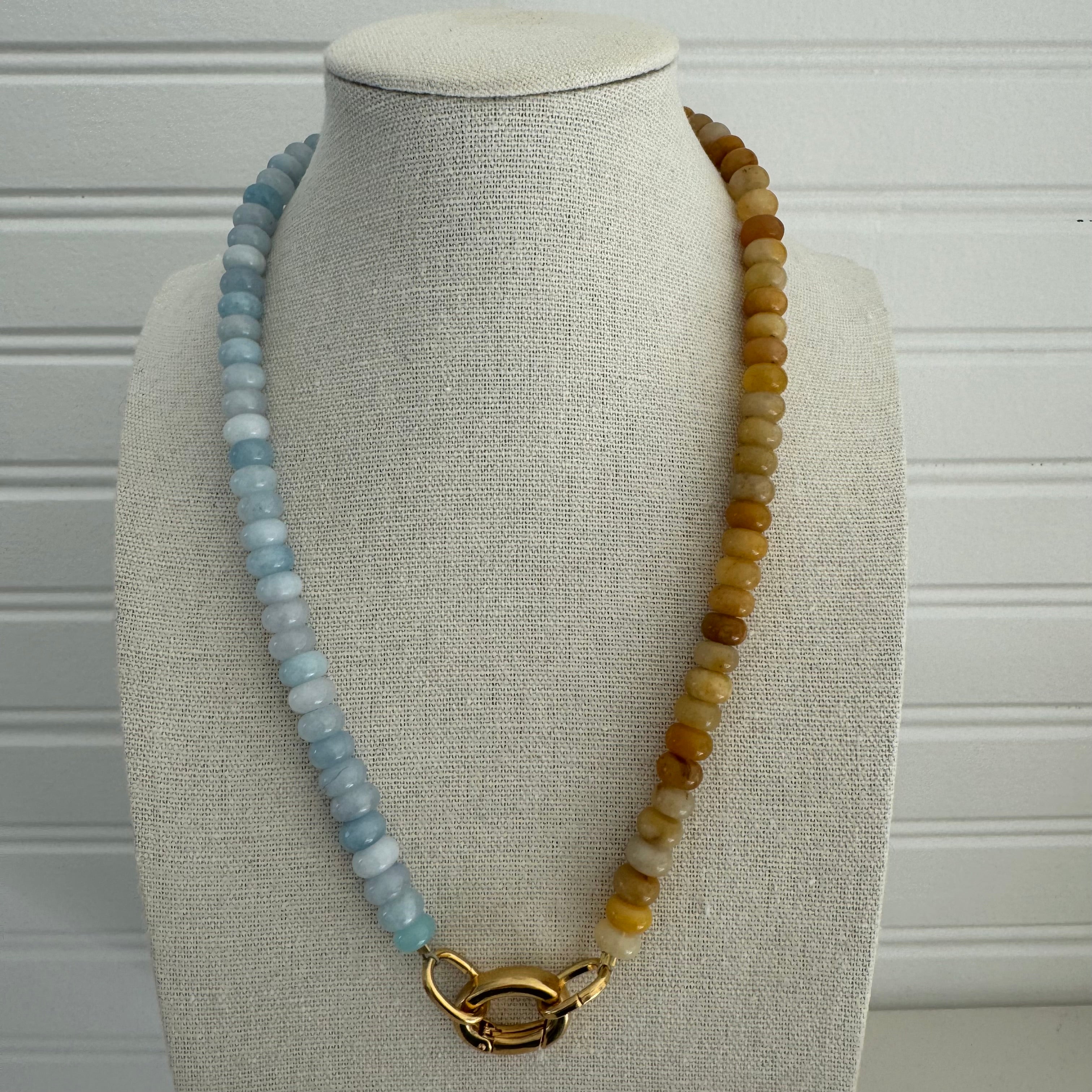 Picture of a bead necklace that is half light blue and half dark amber yellow. Necklace has a gold carabiner clasp.