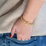 Gold chain bracelet on a wrist with a neutral background
