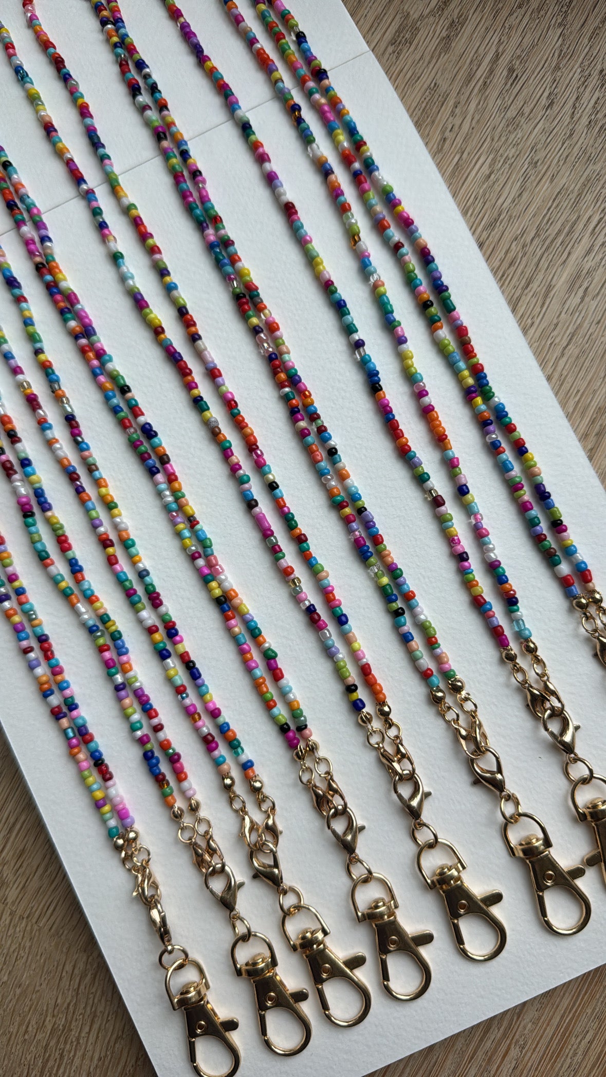 Picture of 8 multicolored beaded lanyards with gold clasps lined up next to each other.
