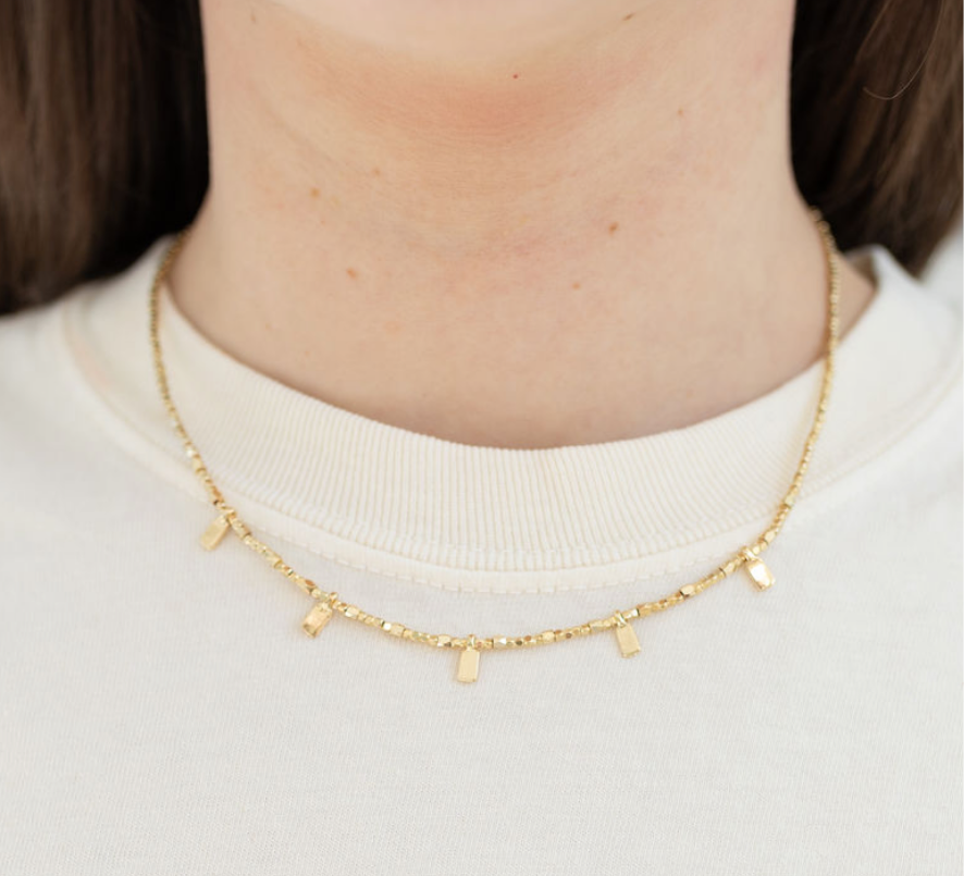 Gold necklace with gold tabs worn by a person on a white background