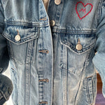 Model displaying a denim jacket with a red heart embroidered on the breast.