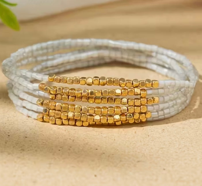 Stack of white and gold beaded bracelets on a beige surface