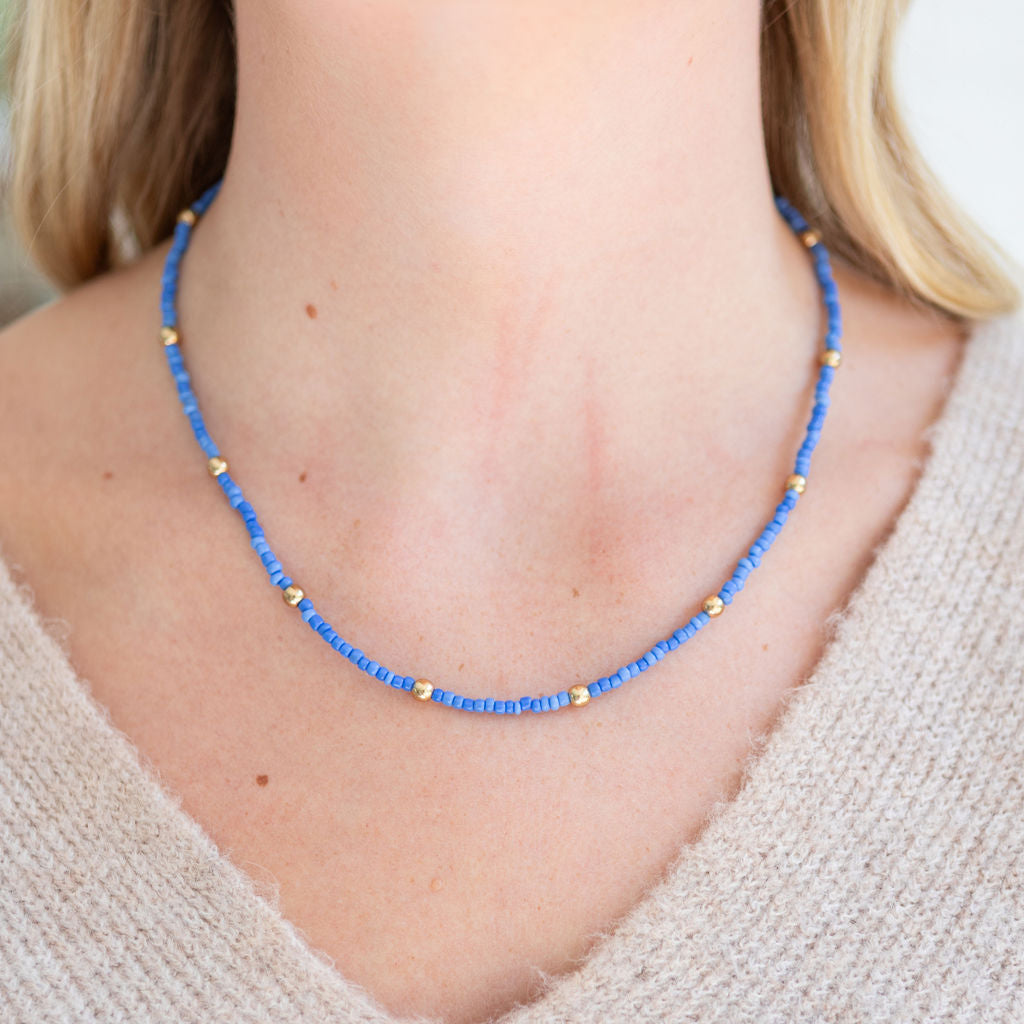 Blue and gold beaded necklace worn by a person with a neutral background
