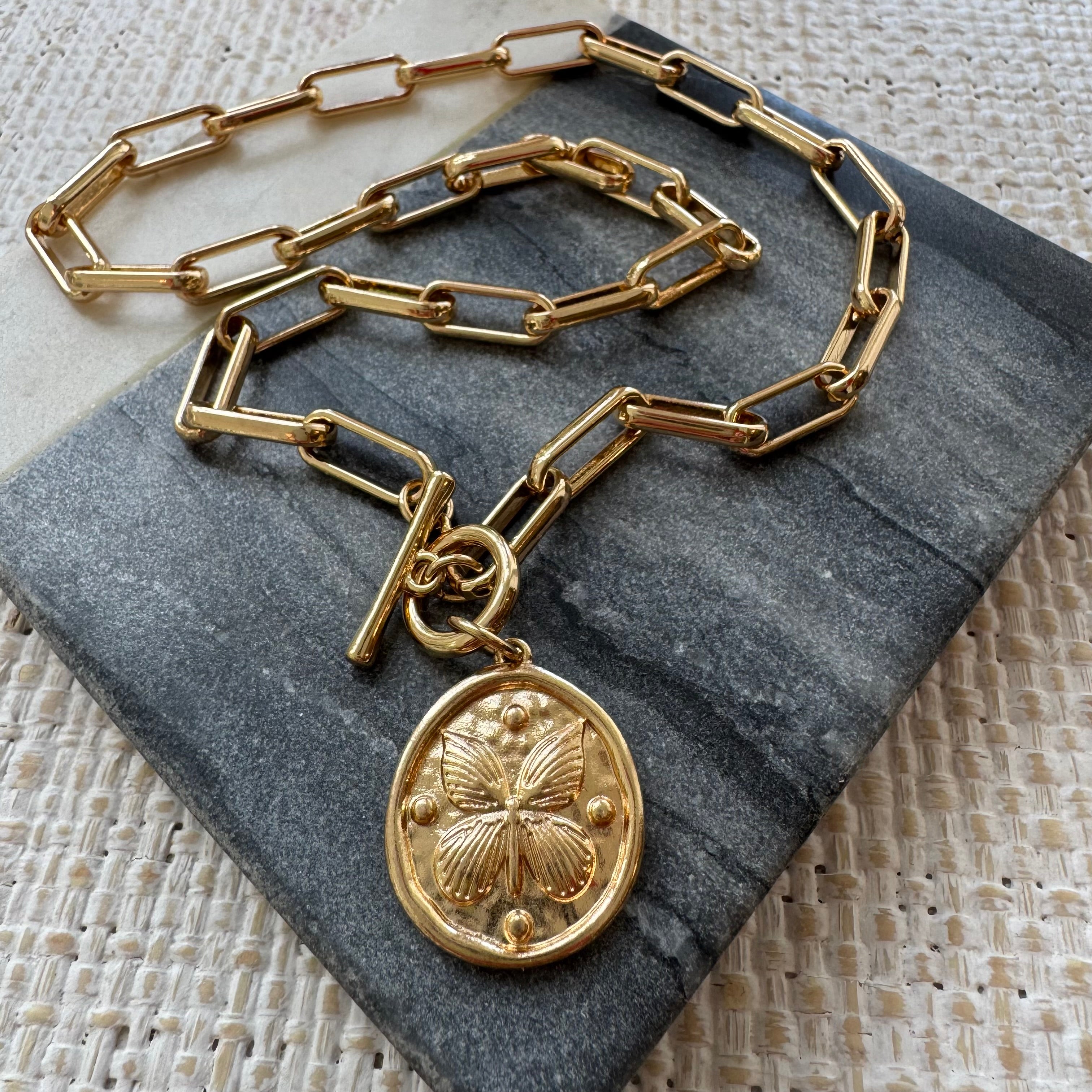 Gold chain necklace with a butterfly pendant on a stone surface