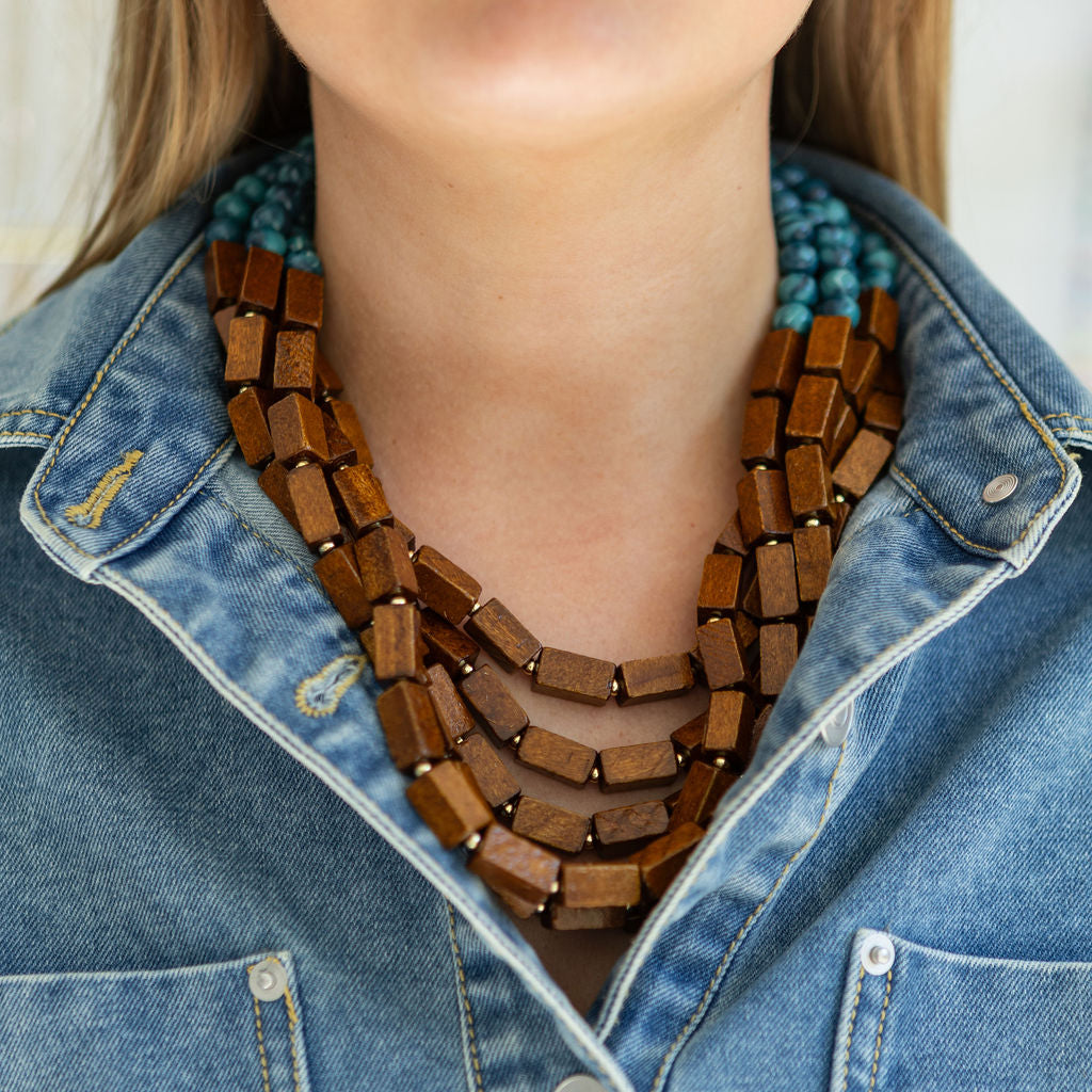 Multi-strand wooden beaded necklace worn by a person with a denim jacket