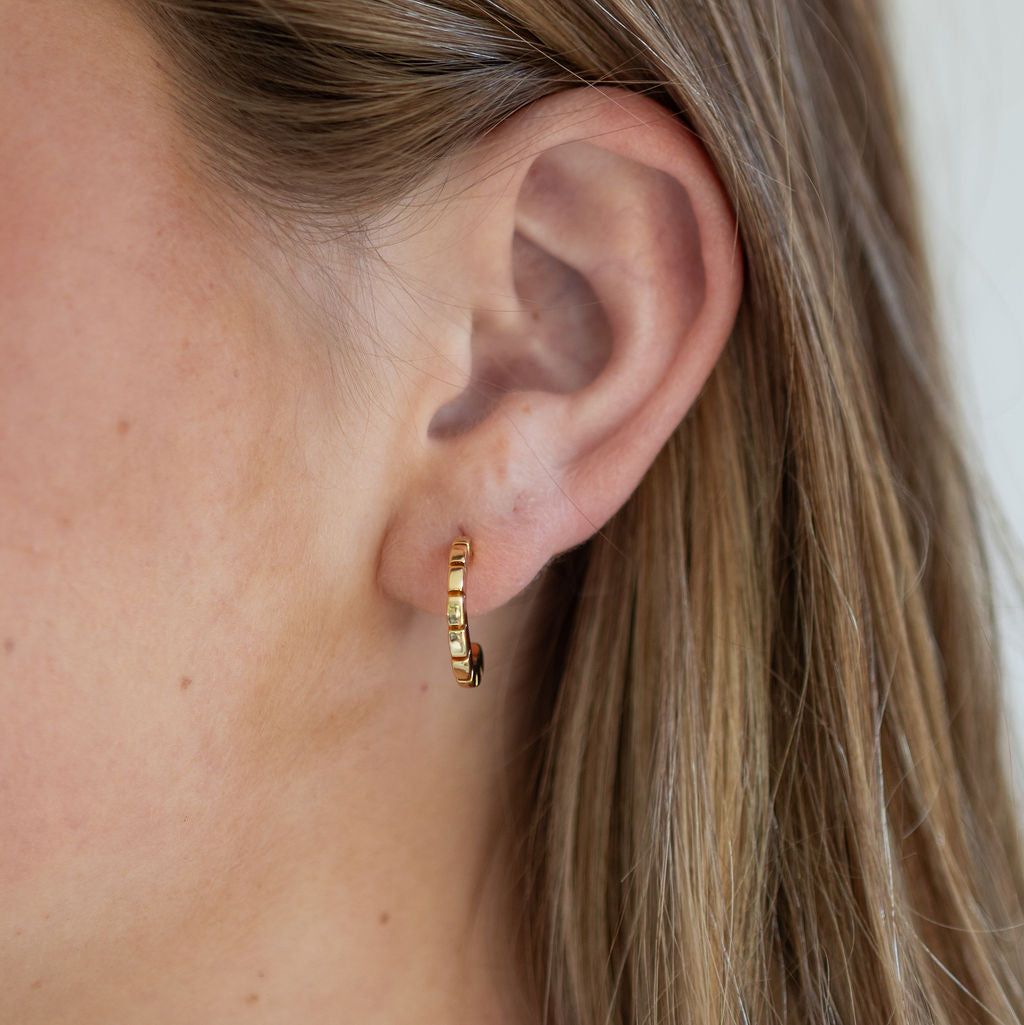 Close-up of a person wearing a gold hoop earring with a neutral background