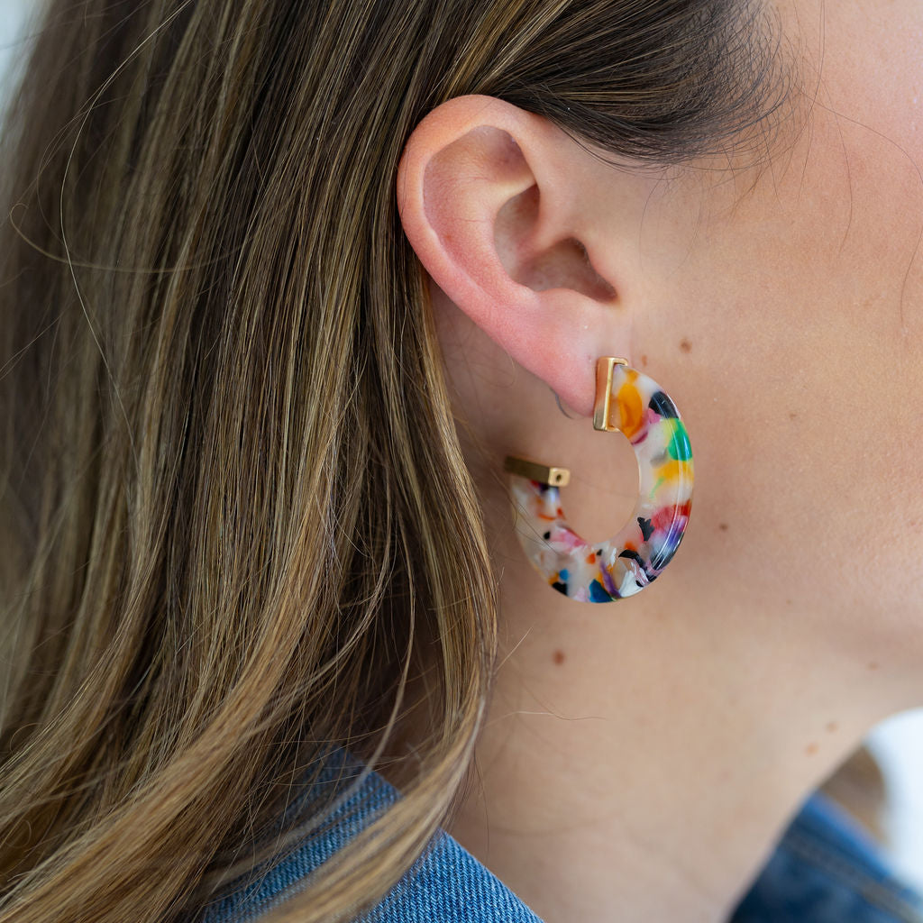 Picture of woman wearing a large multicolored chunky resin hoop earring.