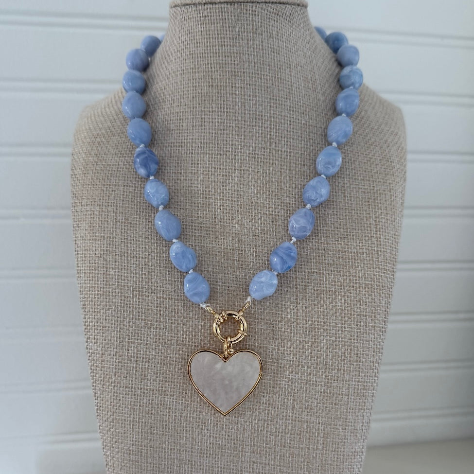 Necklace with blue beads and a gold and white enamel heart-shaped pendant on a mannequin bust.