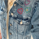 Model wearing a denim jacket with embroidered hearts above the breast pocket