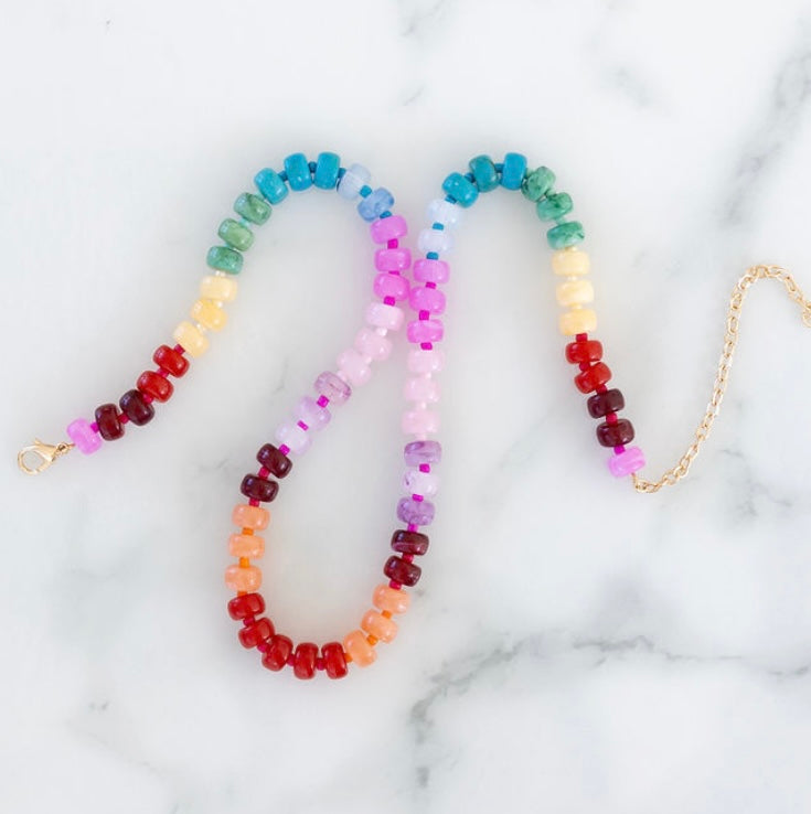 A colorful beaded necklace with a gold-colored clasp, laid out on a marble surface.