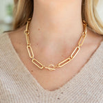 Gold rectangular chain necklace and toggle clasp by a person with a neutral background