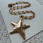 Gold star-shaped pendant on a chain against a textured white background