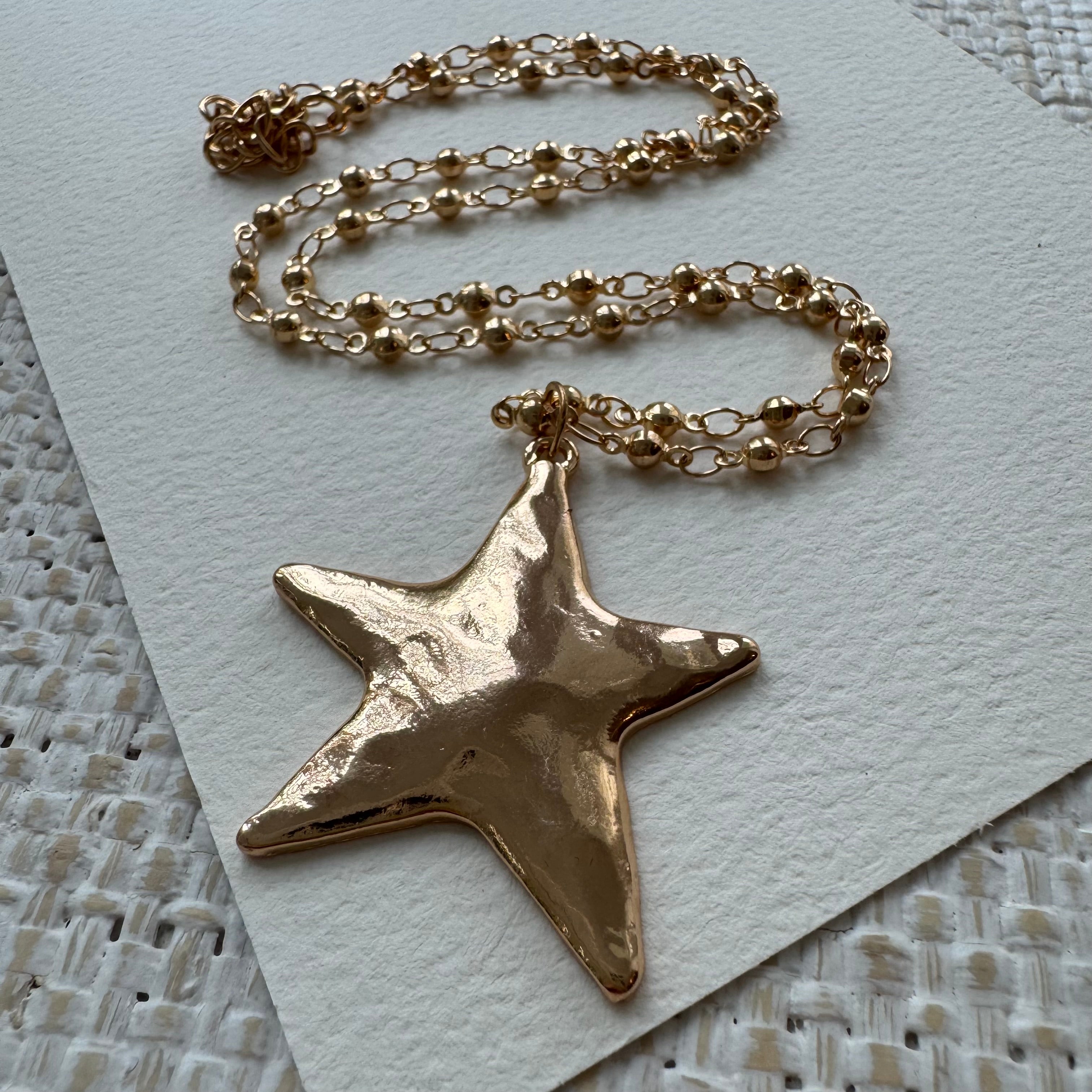 Gold star-shaped pendant on a chain against a textured white background