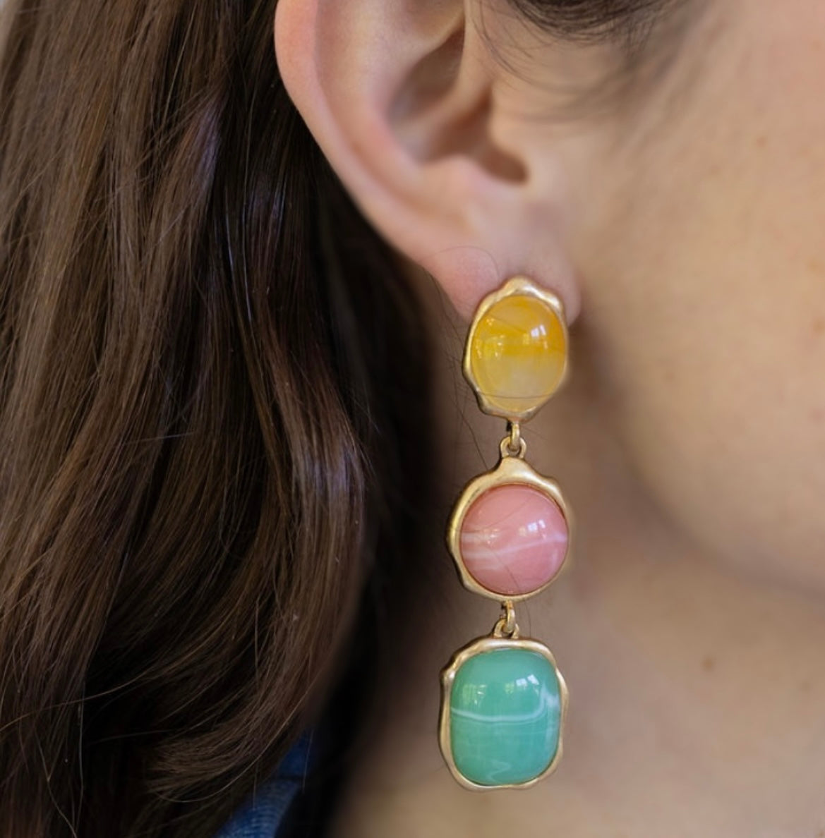 Close-up of an ear wearing a dangling colorful earring with gold accents.