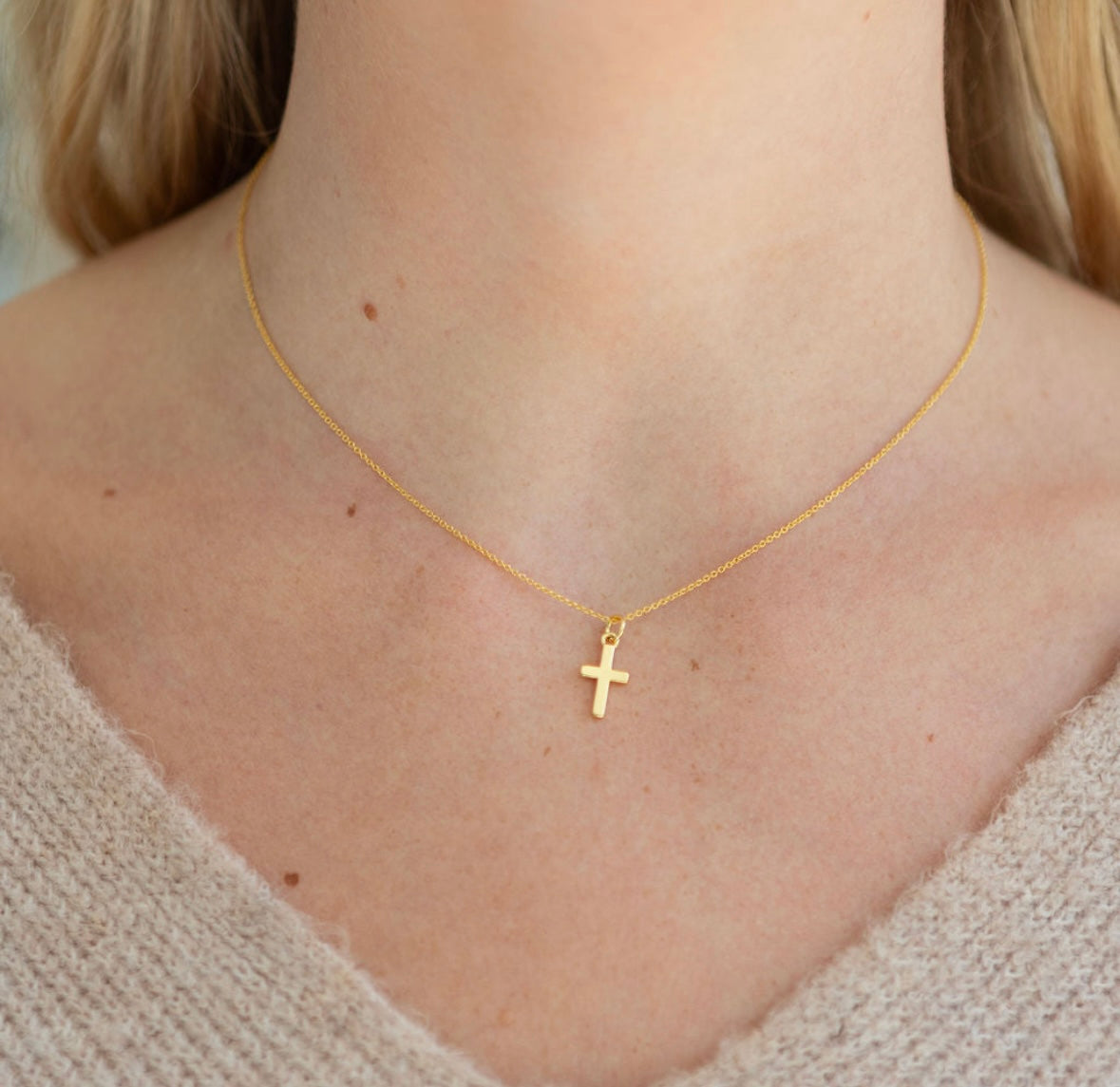 Gold necklace with a cross pendant on a person wearing a beige sweater.