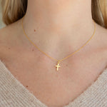 Gold necklace with a cross pendant on a person wearing a beige sweater.