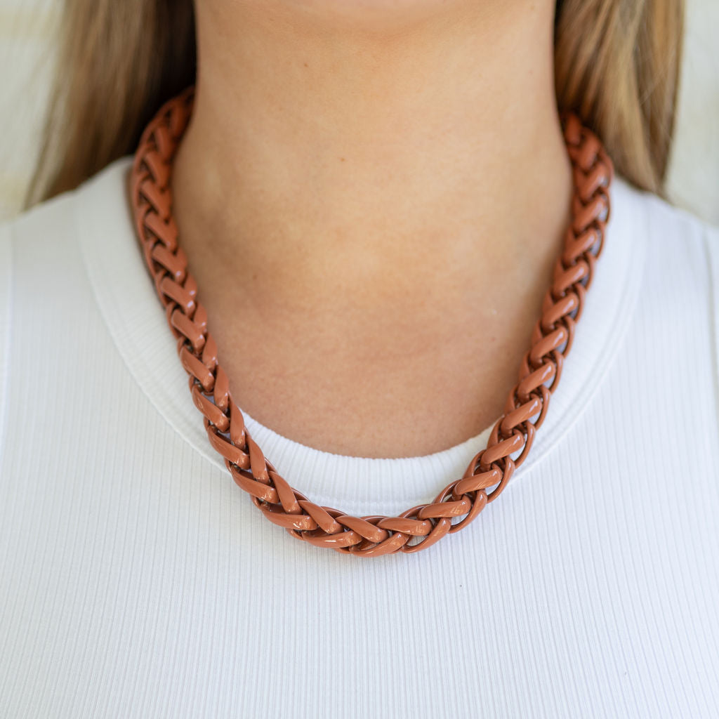 Person wearing a braided brown plastic necklace on a white background