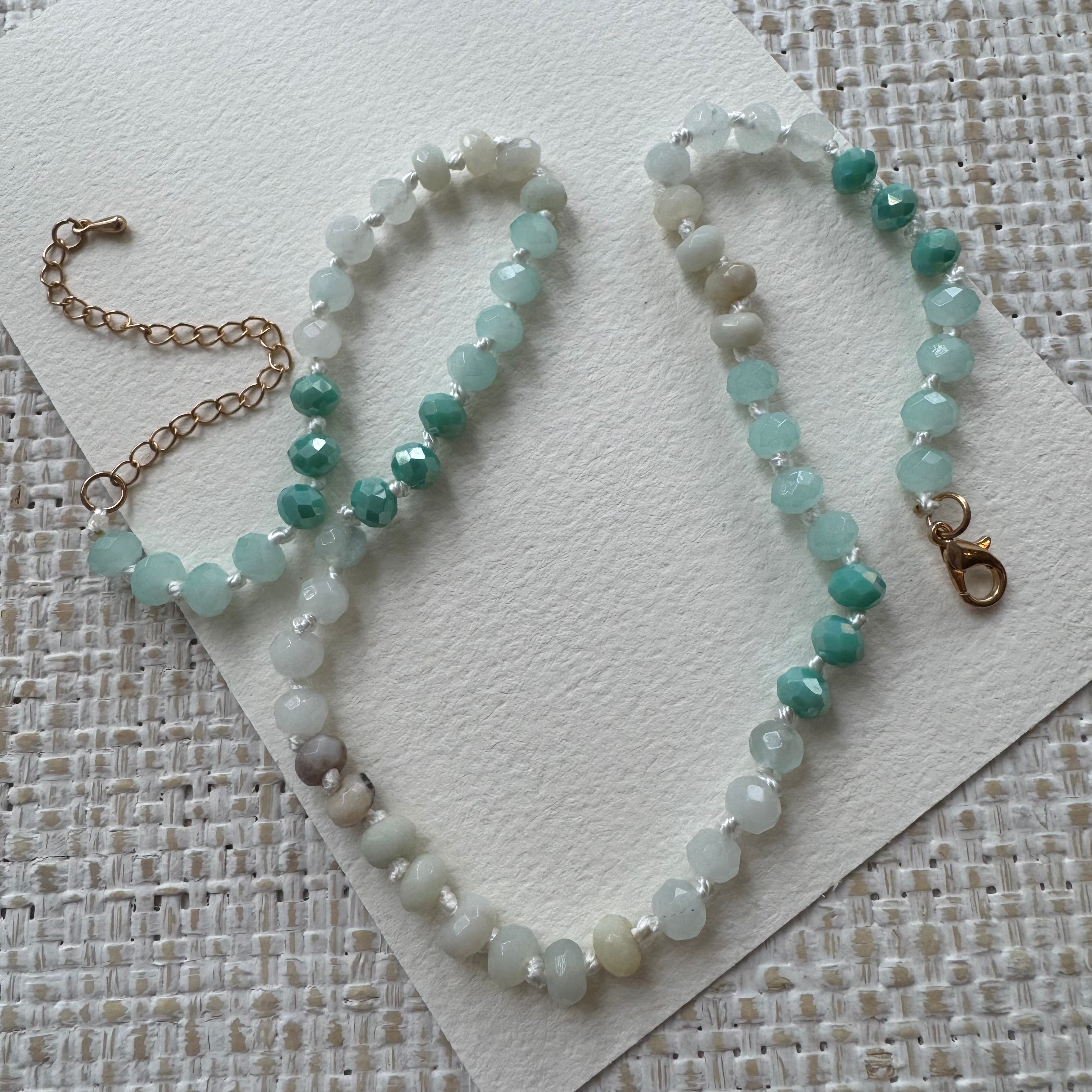 Beaded necklace with green and white stones on a textured surface