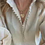 A person wearing a beige shirt and a gold-plated brass toggle necklace with a heart charm.