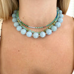 Close-up of a person wearing three beaded necklaces with a neutral background