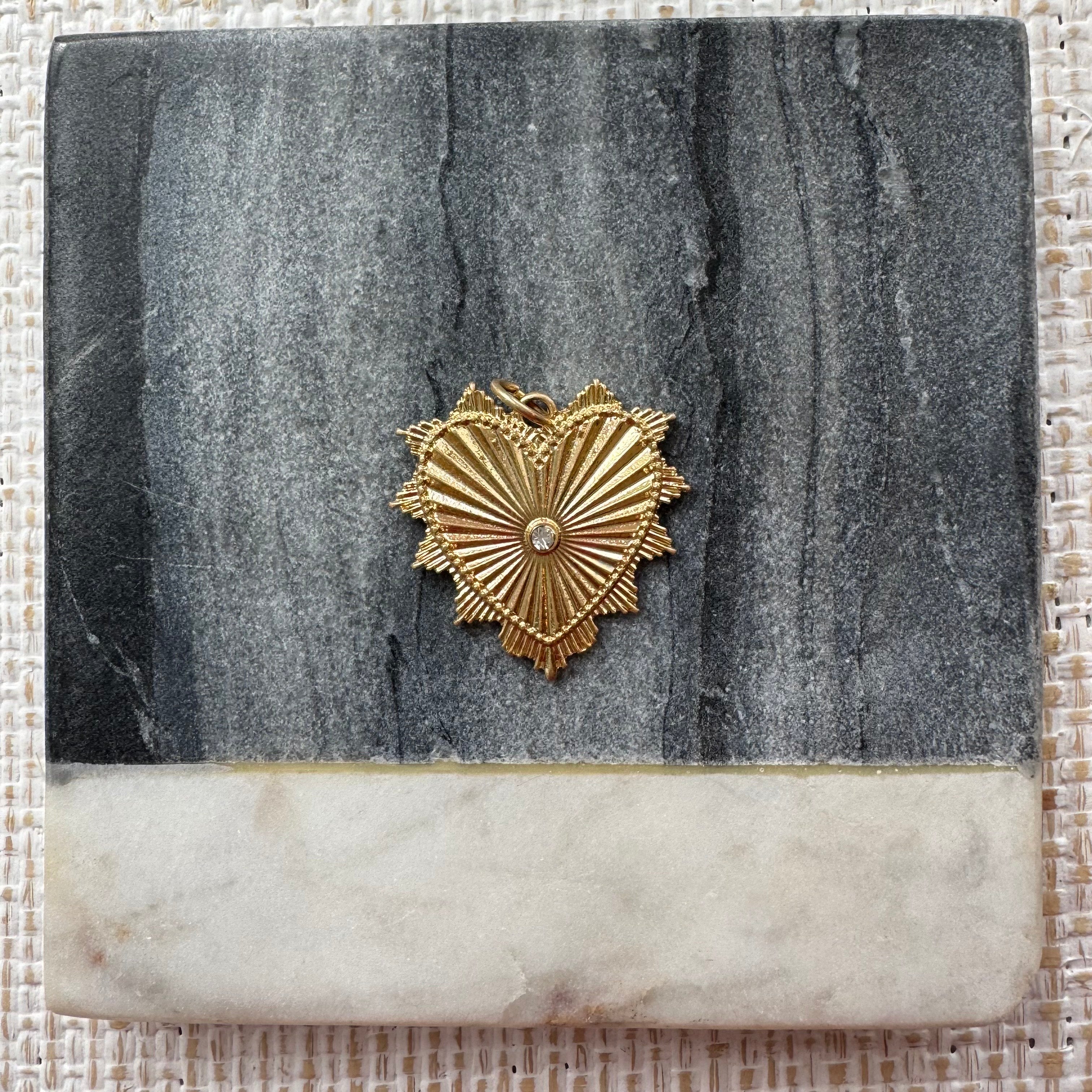 Gold heart pendant with a small clear stone at its center. Heart has an accordion texture and small triangles all around the edge.