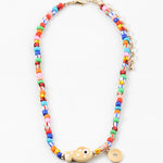 Picture of a bright multi-colored bead necklace with a tan fish bead and a gold disc pendant.