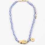 Picture of a bead necklace made of white and blue striped beads and a tan fish bead with a gold disc pendant.