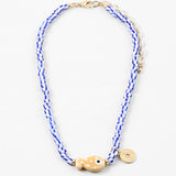 Picture of a bead necklace made of white and blue striped beads and a tan fish bead with a gold disc pendant.