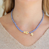 Necklace with tan fish charm and blue and white striped bead necklace worn by a person