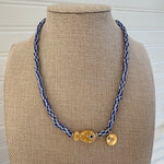 Bead necklace made of white and black striped beads with a tan polka dot fish bead at the center and a small gold disc pendant.