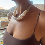 Close-up of a person wearing a beige large stone bead statement necklace with a blurred background