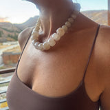 Close-up of a person wearing a beige large stone bead statement necklace with a blurred background