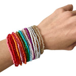 Hand wearing multiple colorful beaded bracelets on a white background