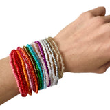 Hand wearing multiple colorful beaded bracelets on a white background