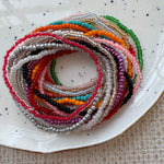 Stack of colorful beaded bracelets on a white plate with a textured surface.